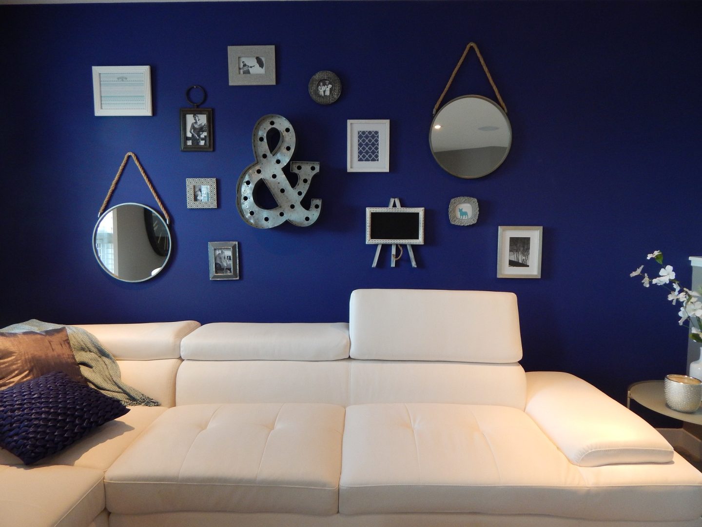 A blue wall features a white couch and a mirror, creating a modern and stylish living space.